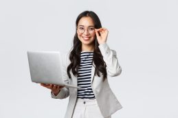 Uma mulher empreendedora de pé sorrindo, por ter aproveitado a Blue Friday, usando um notebook e segurando um par de óculos