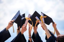 Um grupo de pessoas levantando os capelos e apontando o diploma, representando uma formatura da graduação