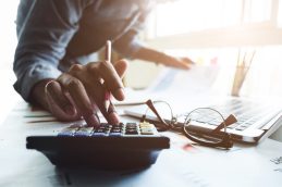 Mão de empresário segurando uma caneta e digitando na calculadora, que está preparando-se para o exame CFC