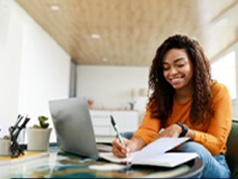 Jovem aplicando dicas práticas para aumentar a eficiência dos estudos online e estudando em frente ao notebook enquanto faz anotações no caderno.