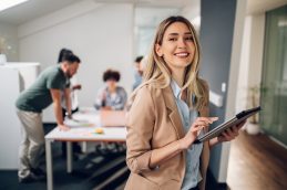 Uma mulher segurando um tablet e sorrindo, representando a profissional de administração que está ajudando a empresa a ser bem-sucedida